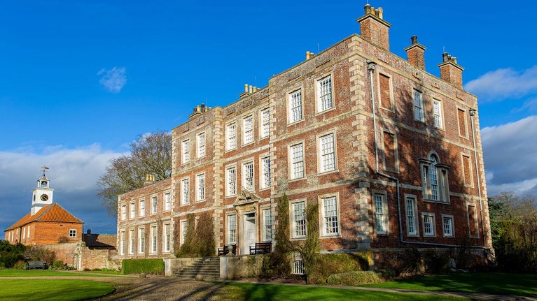The house at Gunby surrounded by green nature and sunlight with the clock tower in the background